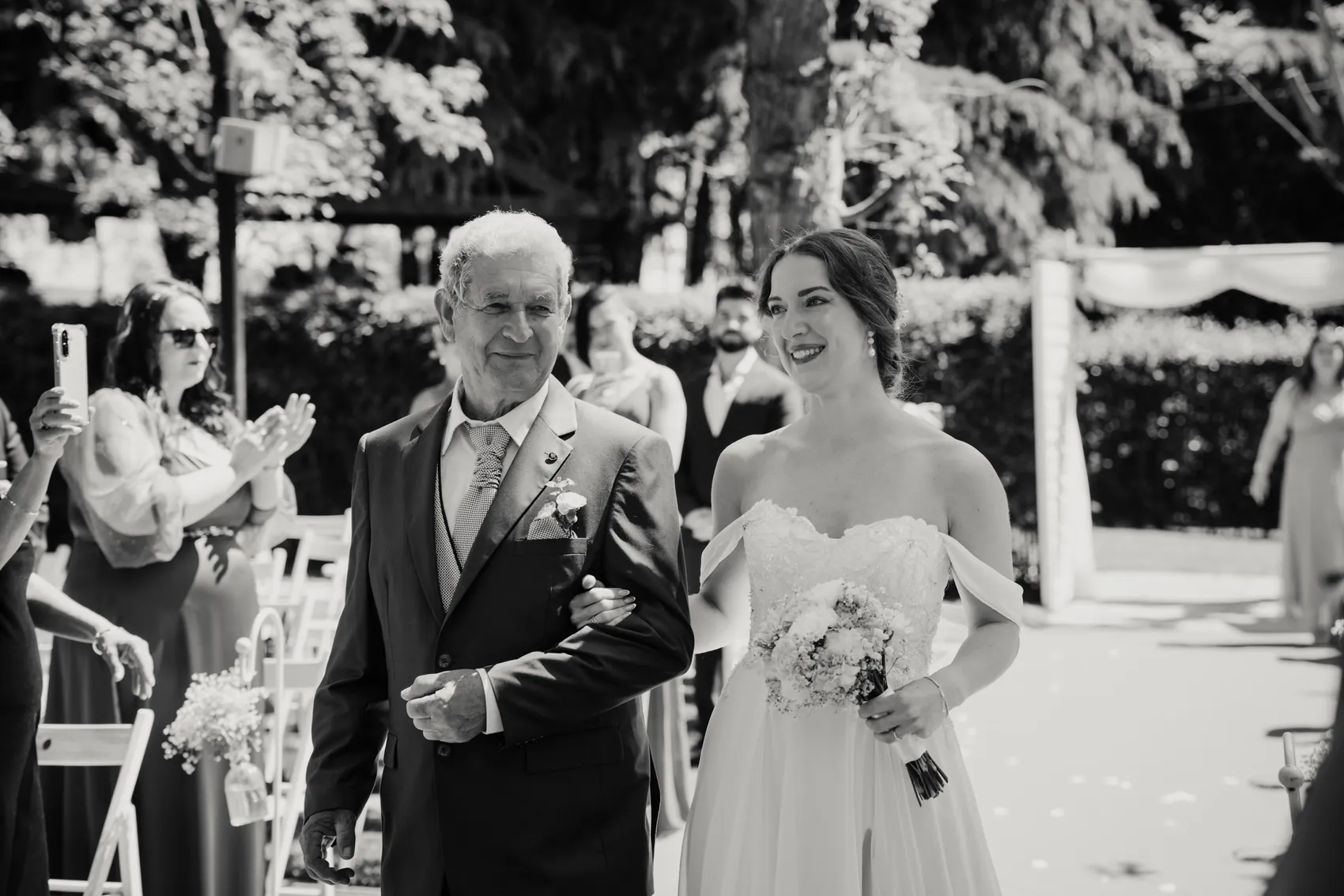 Irene entra del brazo de su padre entre los invitados, en blanco y negro